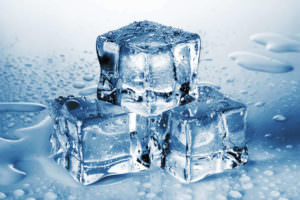 Three clear ice cubes stacked on a wet surface with water droplets surrounding them.