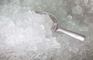 A metal scoop partially buried in a pile of ice cubes.