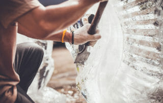Person wearing gloves using a chisel and hammer to sculpt a block of ice.
