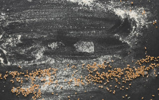 Black surface with scattered flour and wheat grains.