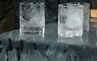 Three ice glasses sit on an icy surface, with frost and ice formations visible inside and outside the glasses.