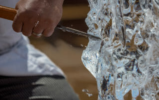 A person carves an intricate design into a block of ice using a chisel.