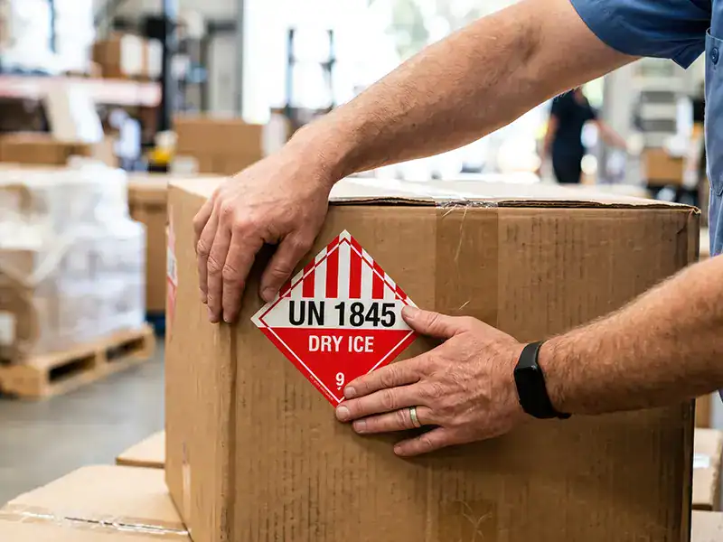 A man places a warning label on a box with dry ice